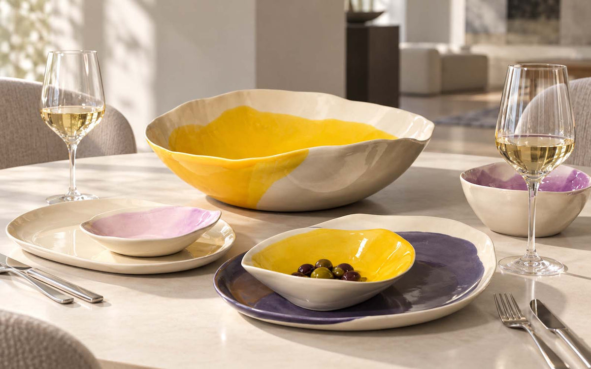 Table setting with handmade yellow and aubergine ceramic plates and serving bowls
