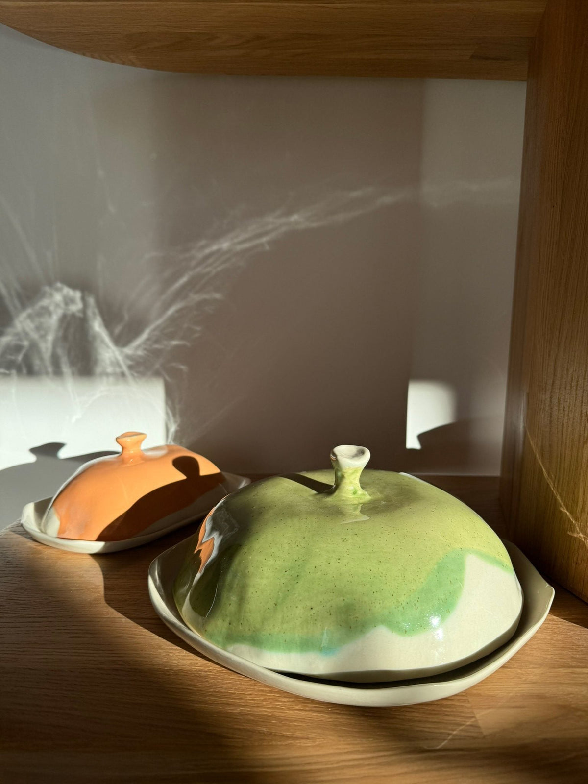 Green lidded ceramic cheese box with other handmade dishes on a sunlit table