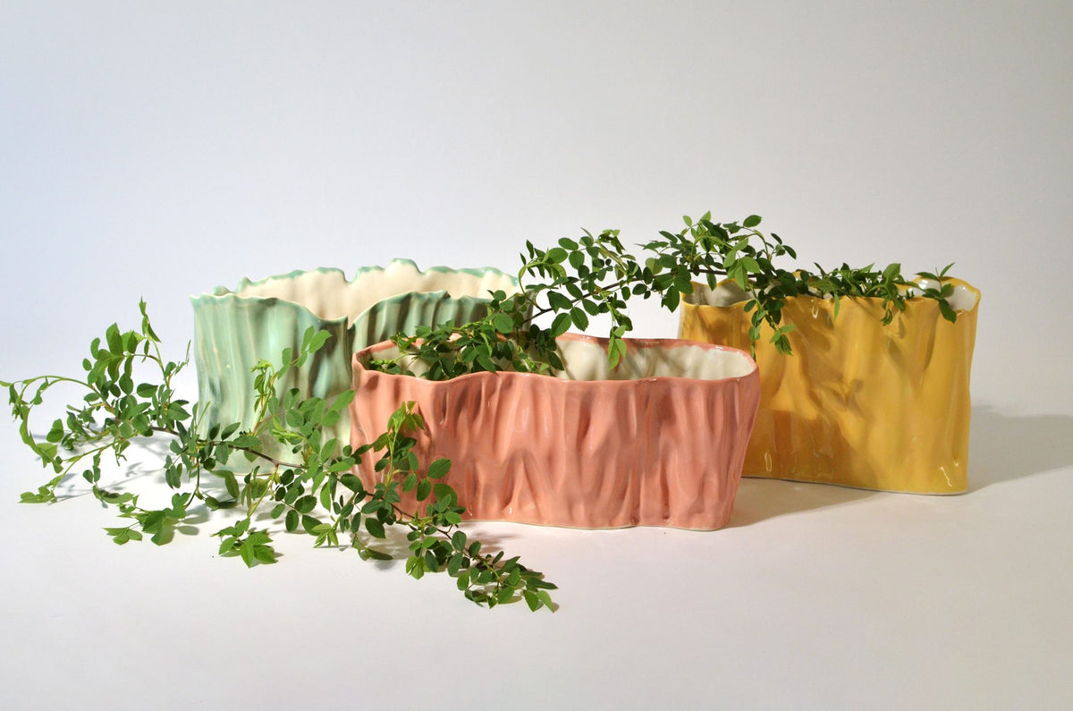 Green, pink and yellow wide ceramic vases arranged with foliage