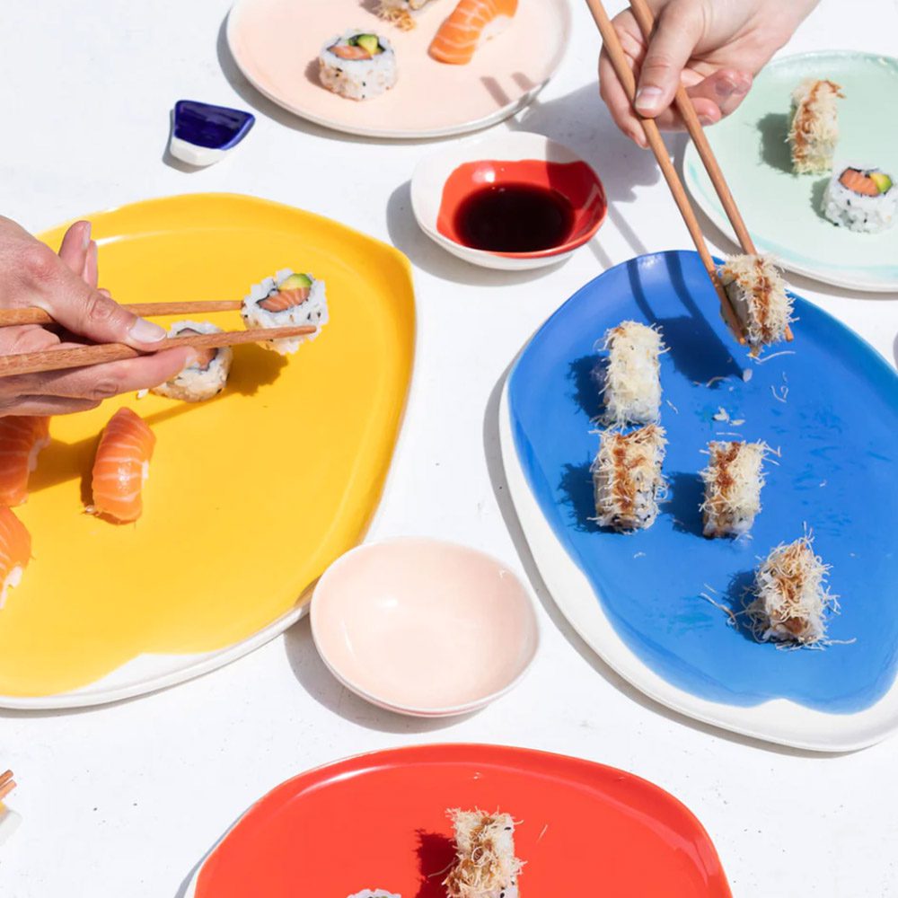 Sushi shared on handmade yellow, blue and red plates with small dip bowls, seen from above