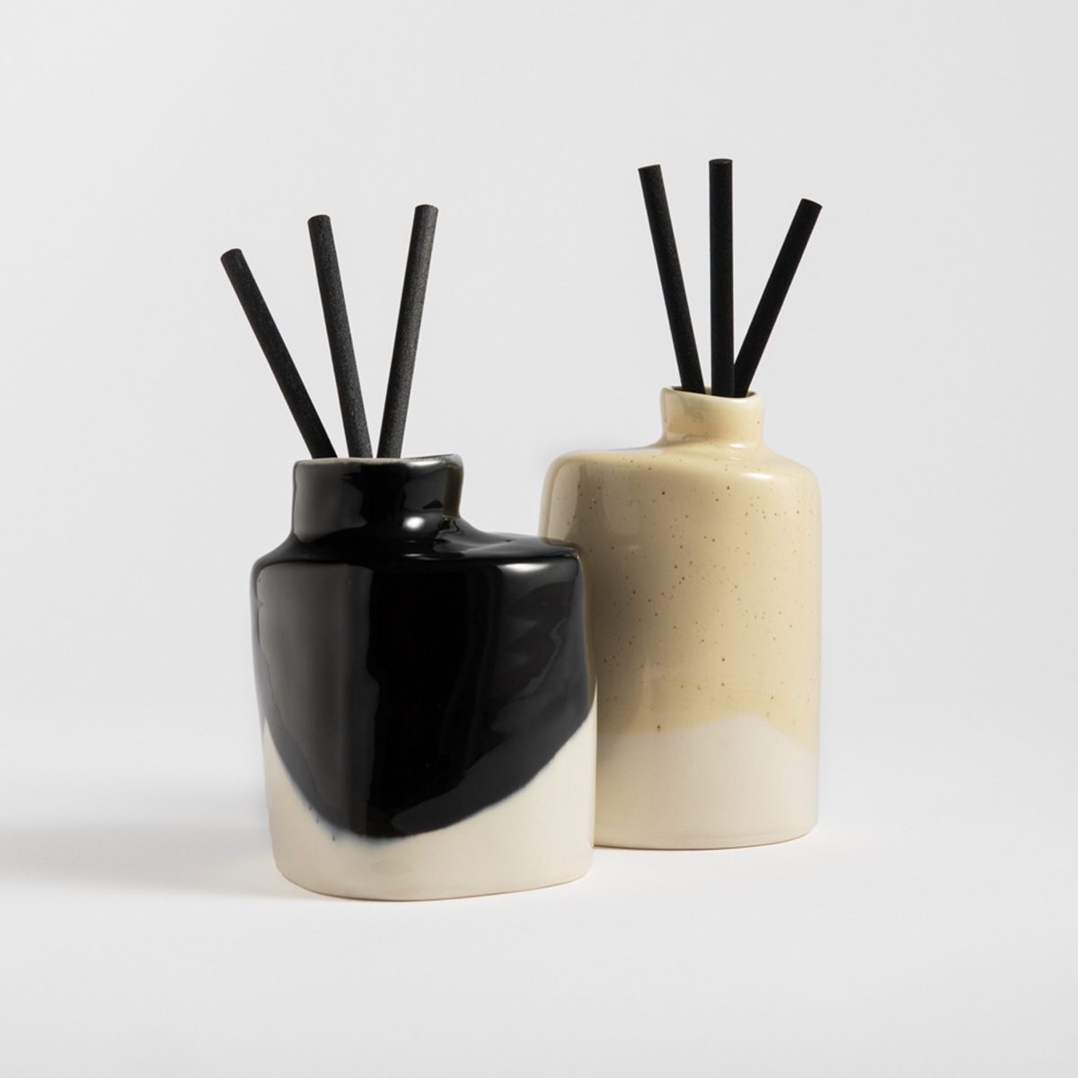 Two handmade porcelain scent diffusers in black and cream colors with black reeds.
