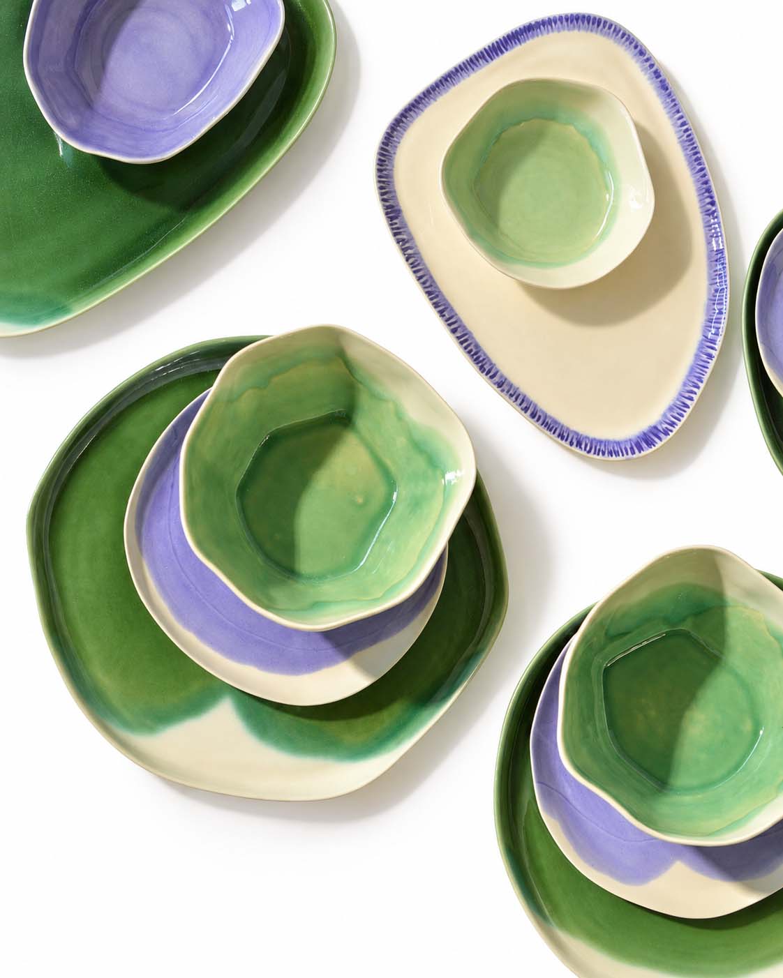 Handmade dining plates and bowls in green and aubergine glazes arranged on white