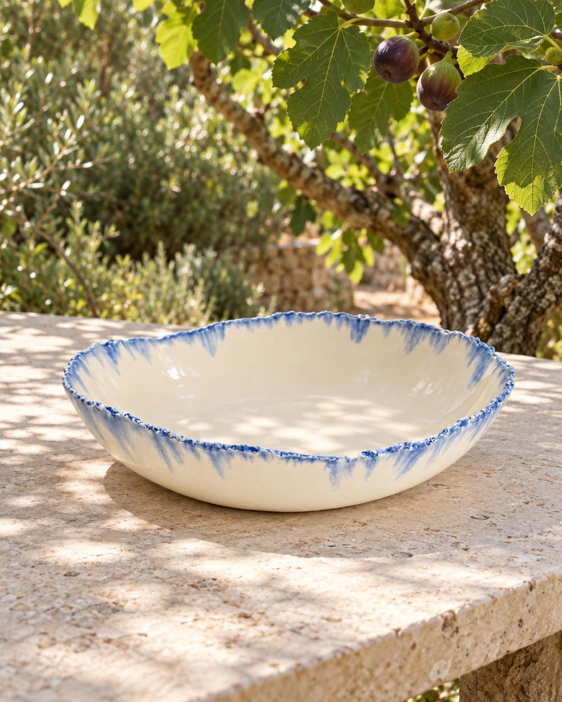 Handmade serving bowl with a sky-blue running glaze rim in a sunlit garden