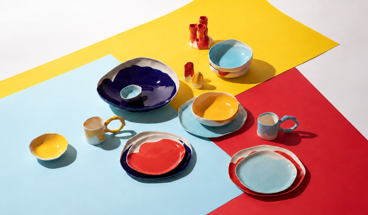 Handmade BAUHAUS plates, bowls and cups arranged across yellow, sky blue and scarlet colour fields