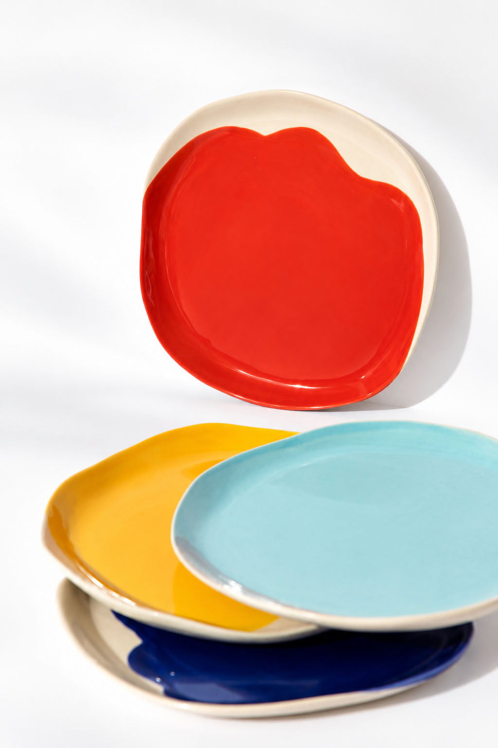 Close view of four BAUHAUS ceramic plates with red, sky blue, yellow and cobalt glazes