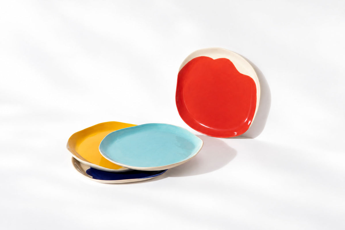 Four BAUHAUS ceramic plates in red, sky blue, yellow and cobalt blue arranged on white