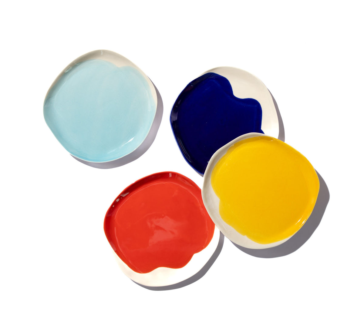 Overhead view of four BAUHAUS ceramic plates in sky blue, cobalt blue, red and yellow on white