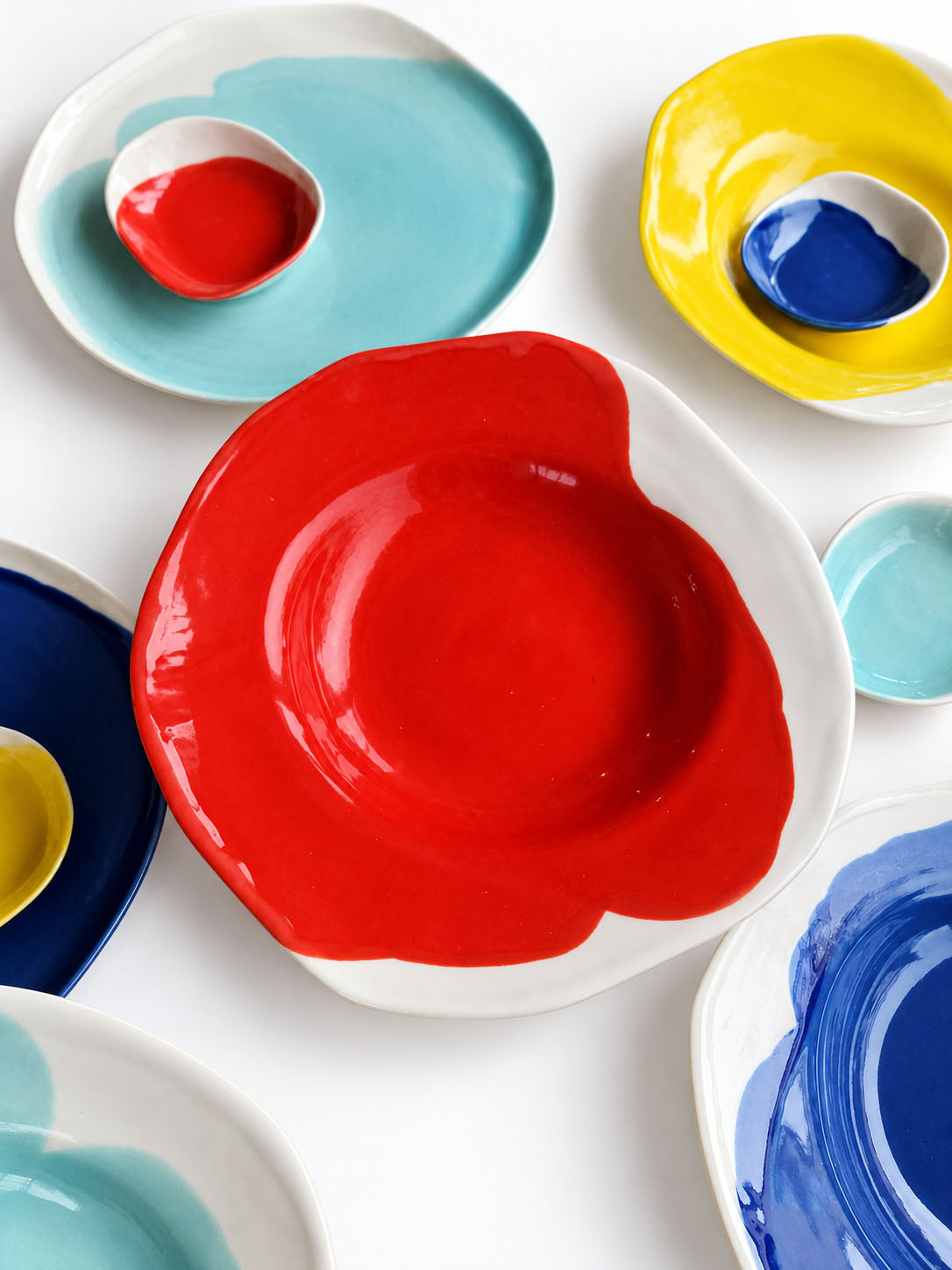 Red BAUHAUS ceramic plate surrounded by colourful plates and small dishes on white