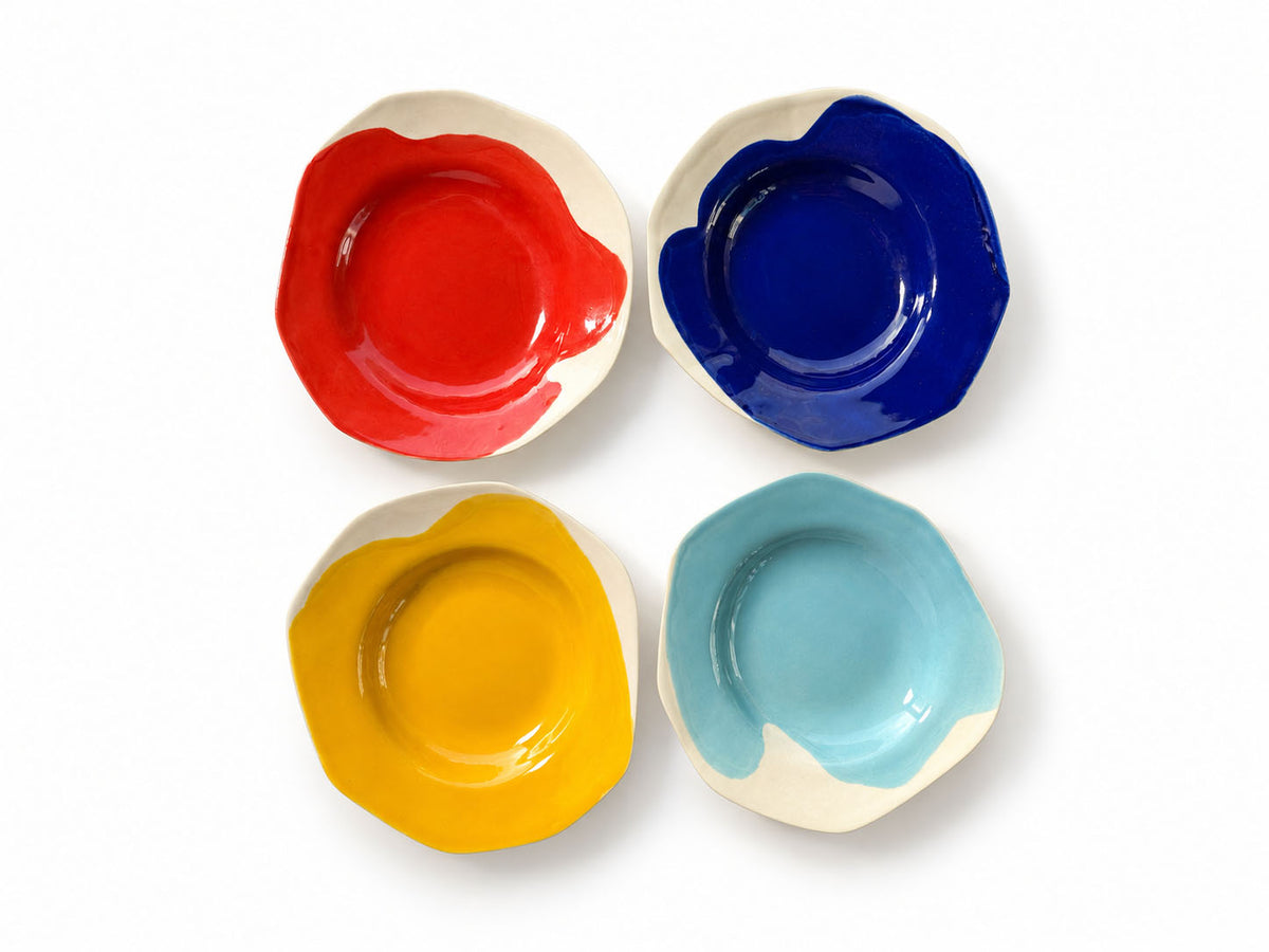Four BAUHAUS deep ceramic plates in red, cobalt blue, yellow and sky blue arranged on white