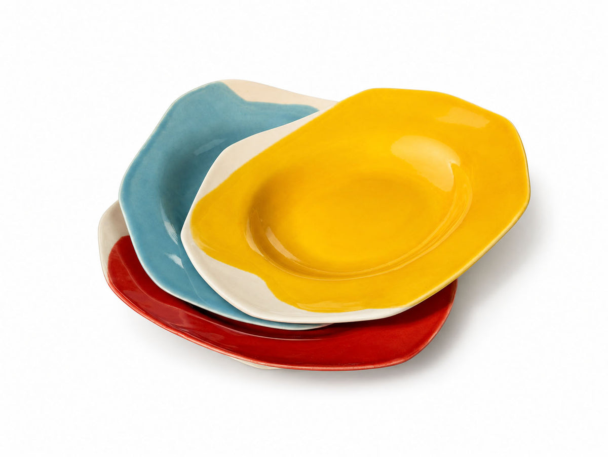 Angled view of stacked BAUHAUS deep ceramic plates in yellow, sky blue, red and cobalt blue