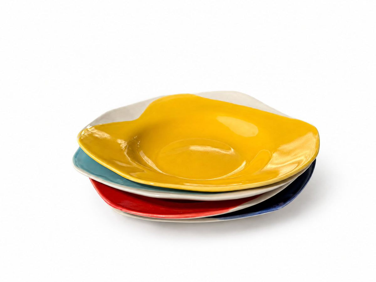 Four stacked BAUHAUS deep ceramic plates with a yellow plate on top on white