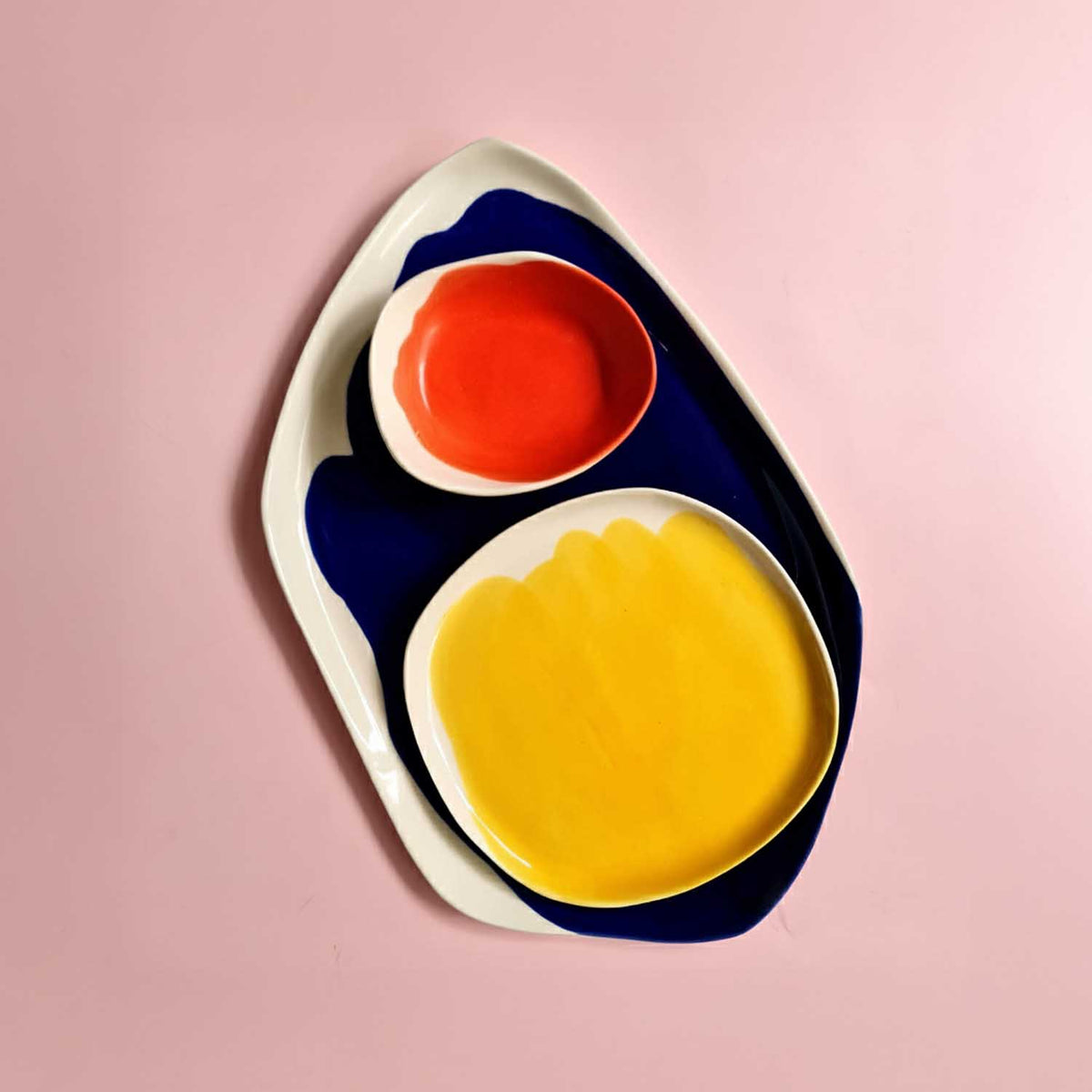 Bauhaus Porcelain Set from above: blue-edged platter with red bowl and yellow plate on pink
