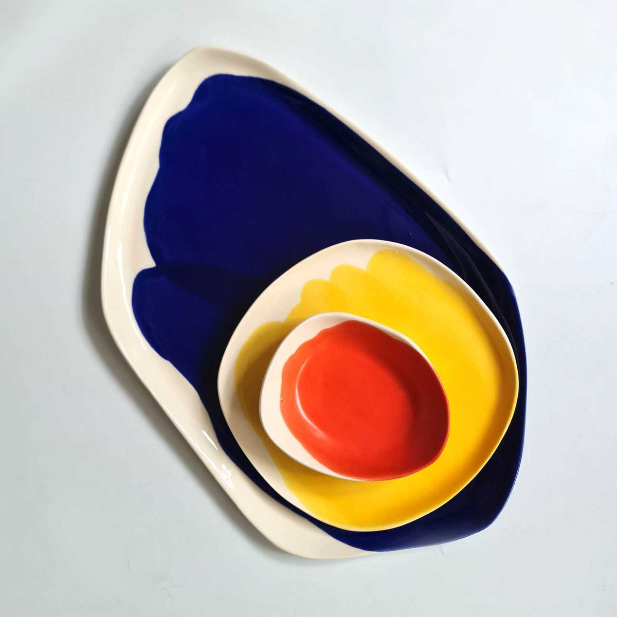 Bauhaus Porcelain Set stacked: red bowl inside yellow plate on an organic royal blue platter