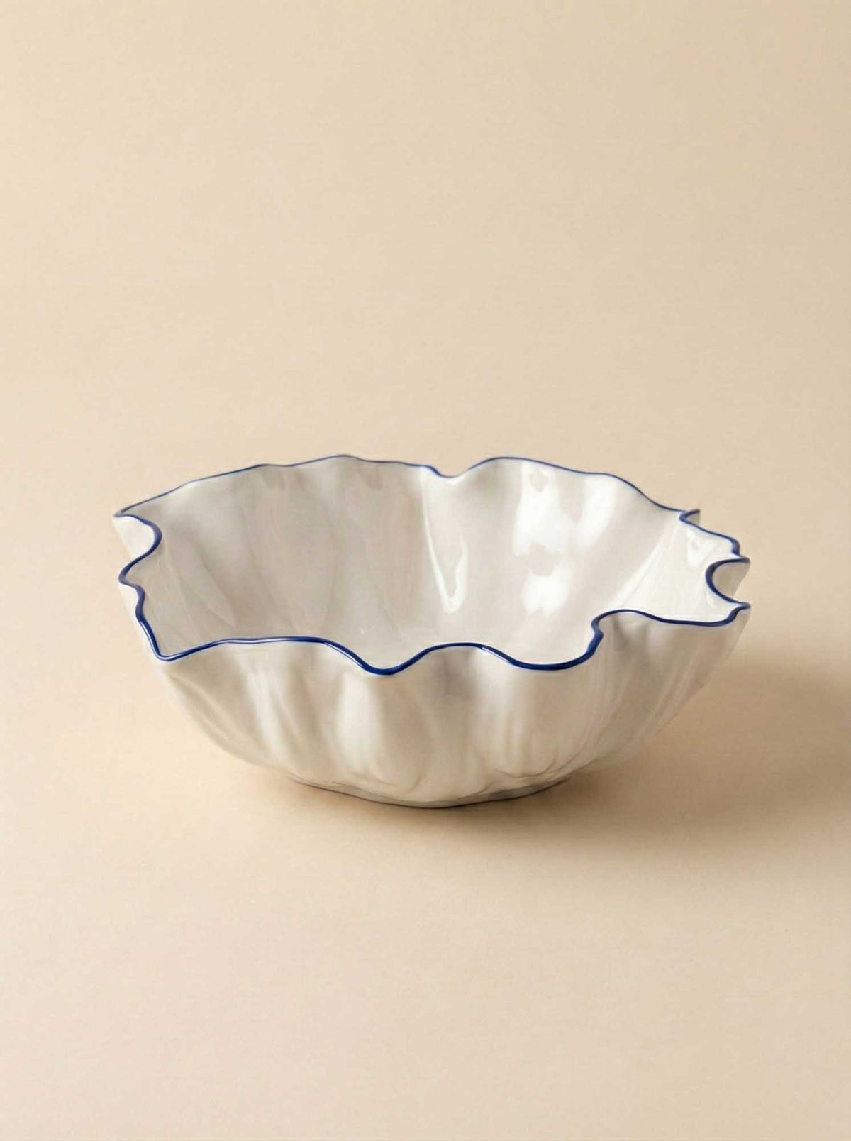 White ruffled Blossom porcelain bowl with a fine blue rim on a beige background