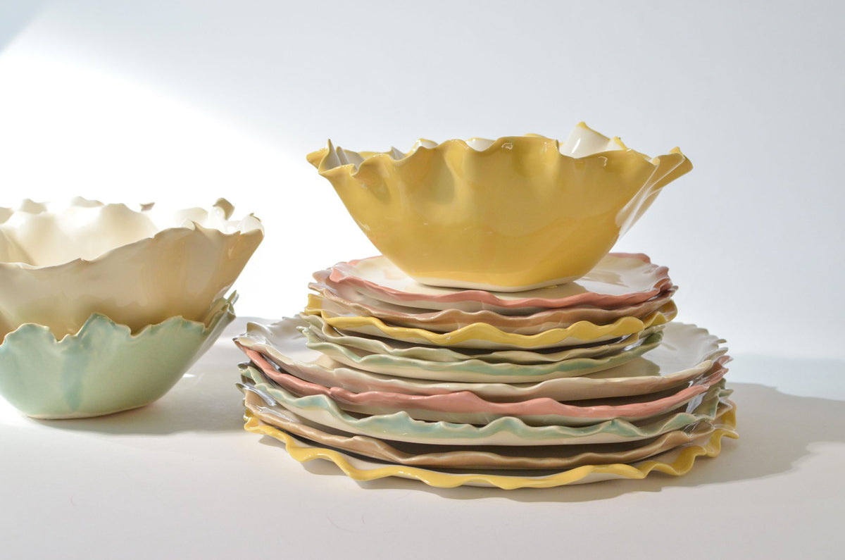 Stacked handmade Blossom plates with folded rims and yellow and green bowls
