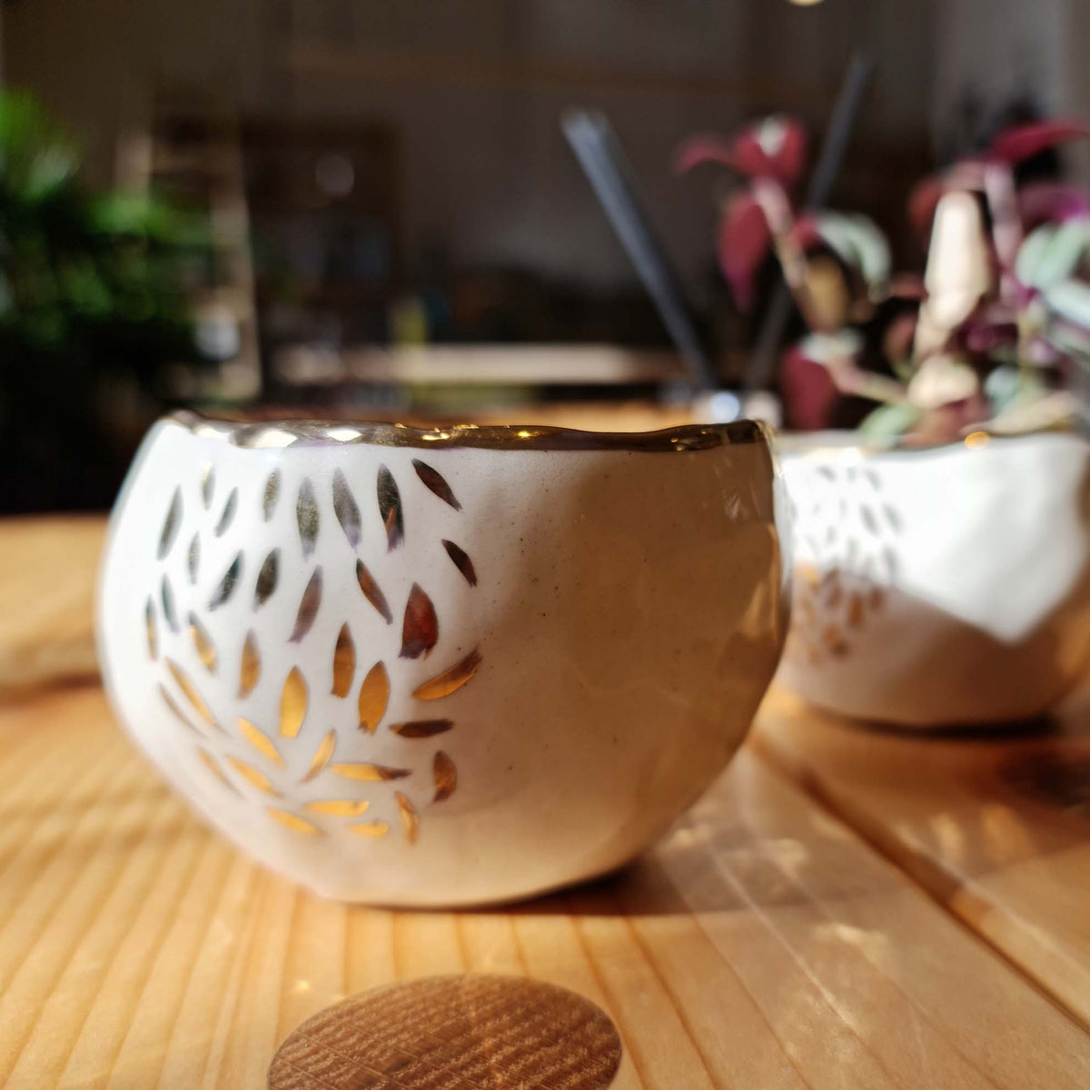 Pinched porcelain cup with hand-painted gold lustre leaf pattern on a wooden table