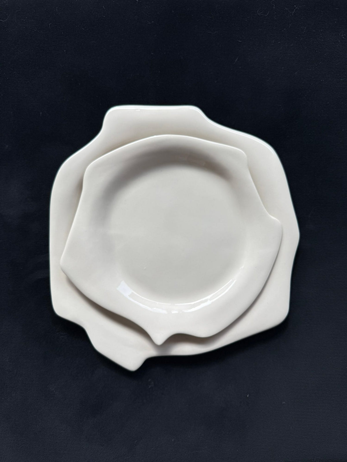 Two stacked white porcelain plates with irregular edges from the Laced collection on a dark background