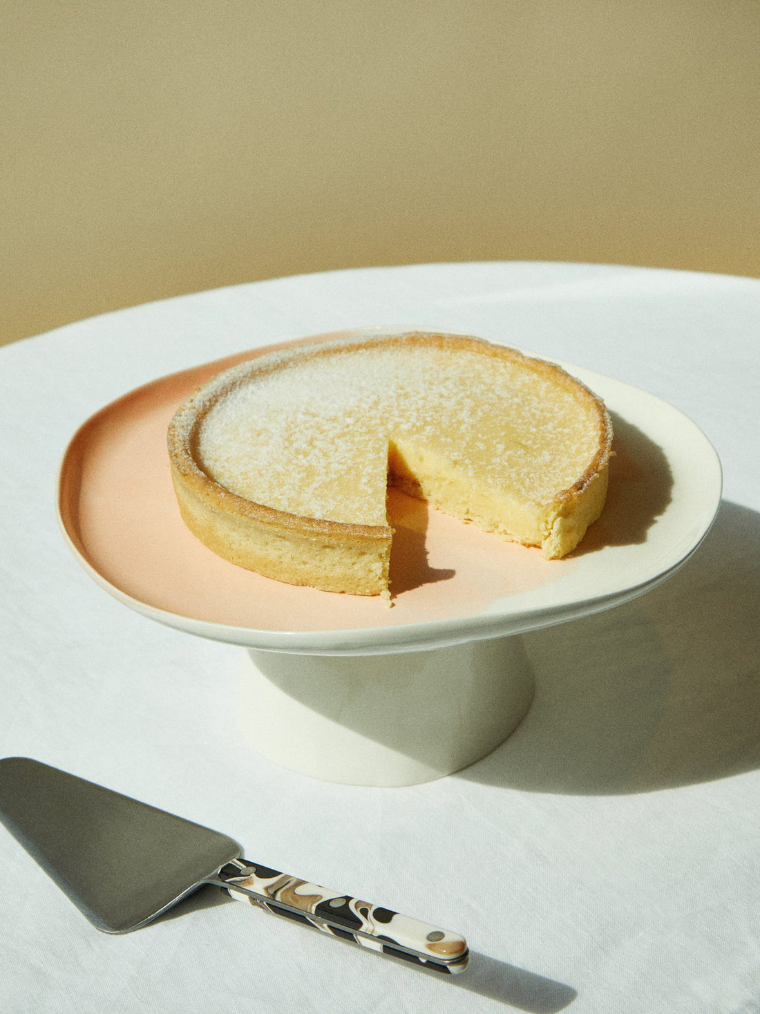 Milky Pink porcelain cake stand with a lemon tart and a cake server on a white table