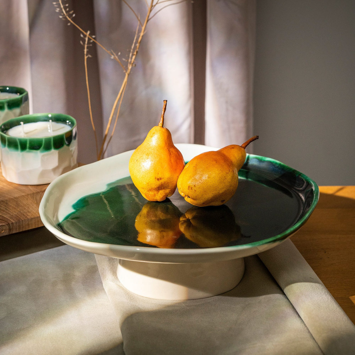 Green ceramic cake stand displaying two yellow pears