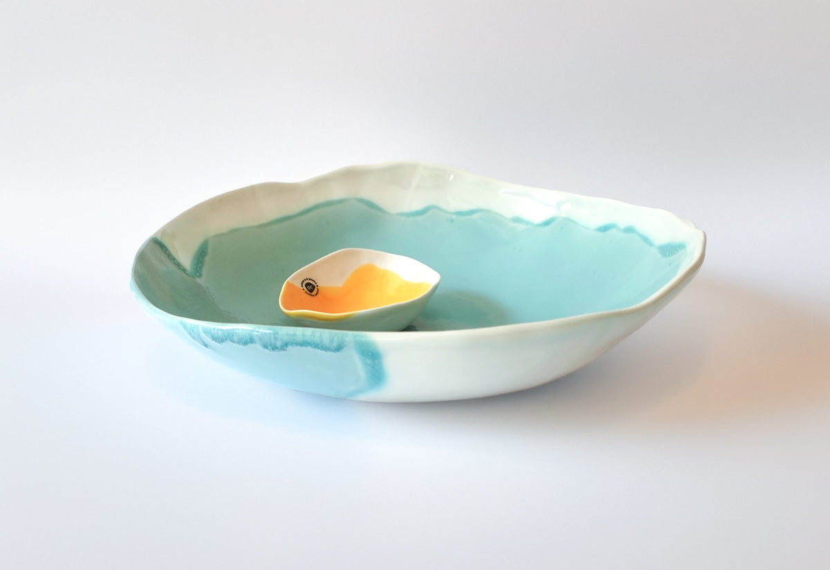 Turquoise porcelain serving bowl with a small yellow dish inside, on a white background