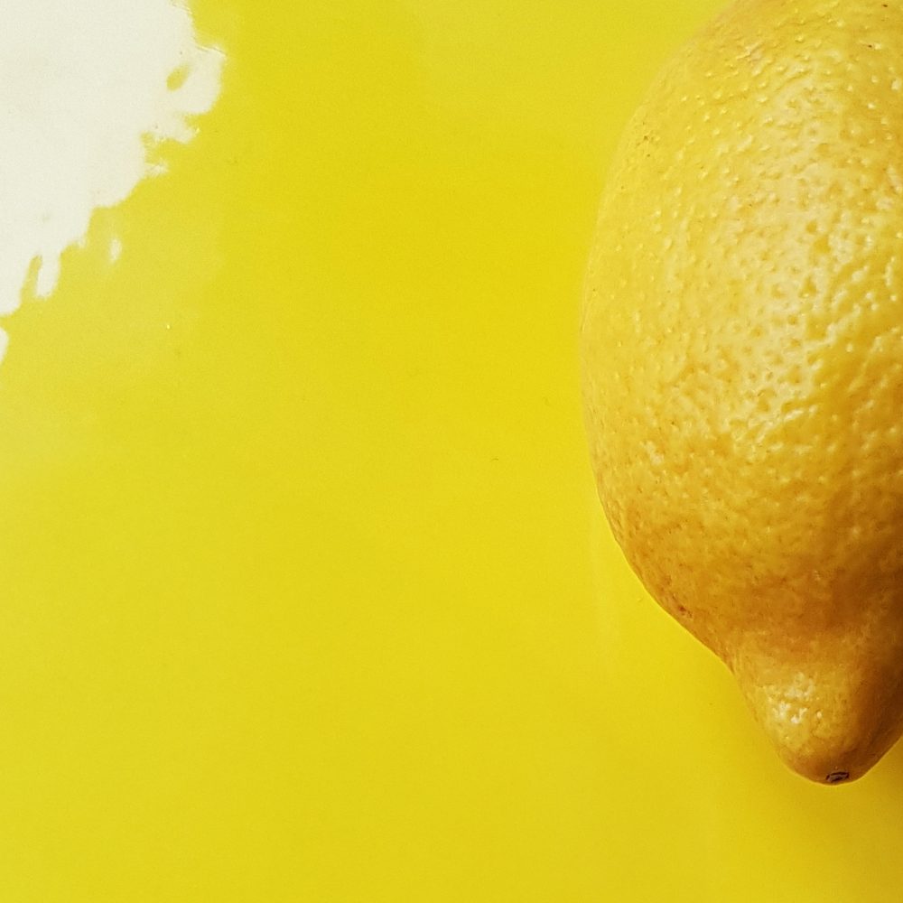 Lemon Yellow glossy glaze sample on handmade porcelain beside a fresh lemon