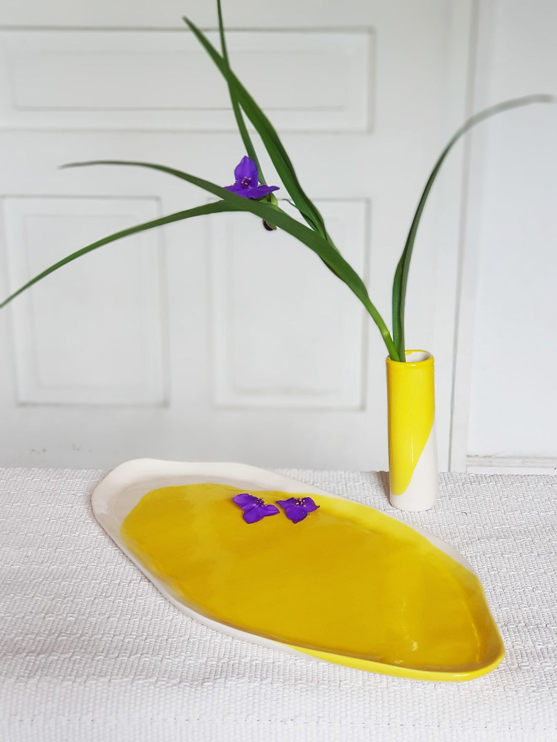 Lemon Yellow porcelain serving platter and slim bud vase holding a purple flower and long leaves