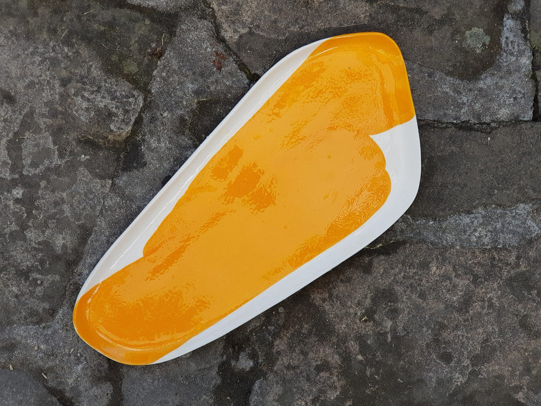 Long handmade porcelain serving platter in Mandarin Orange glaze on a dark stone surface