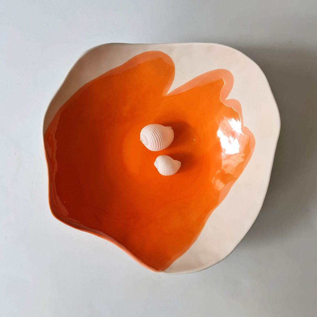 Handmade porcelain bowl in Mandarin Orange glaze with a white rim and two small seashells