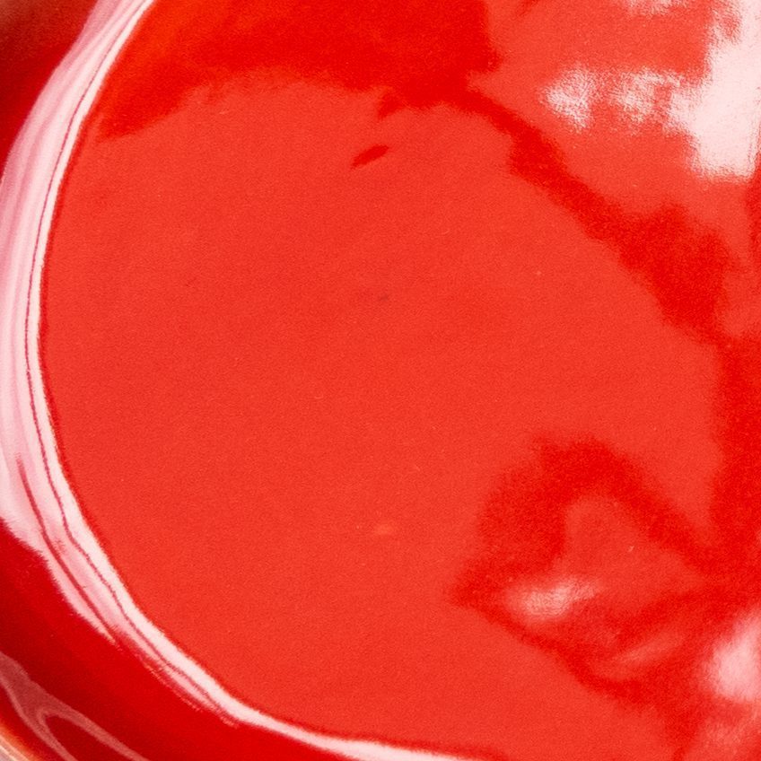 Red Scarlet glossy glaze sample on handmade porcelain with a curved white edge