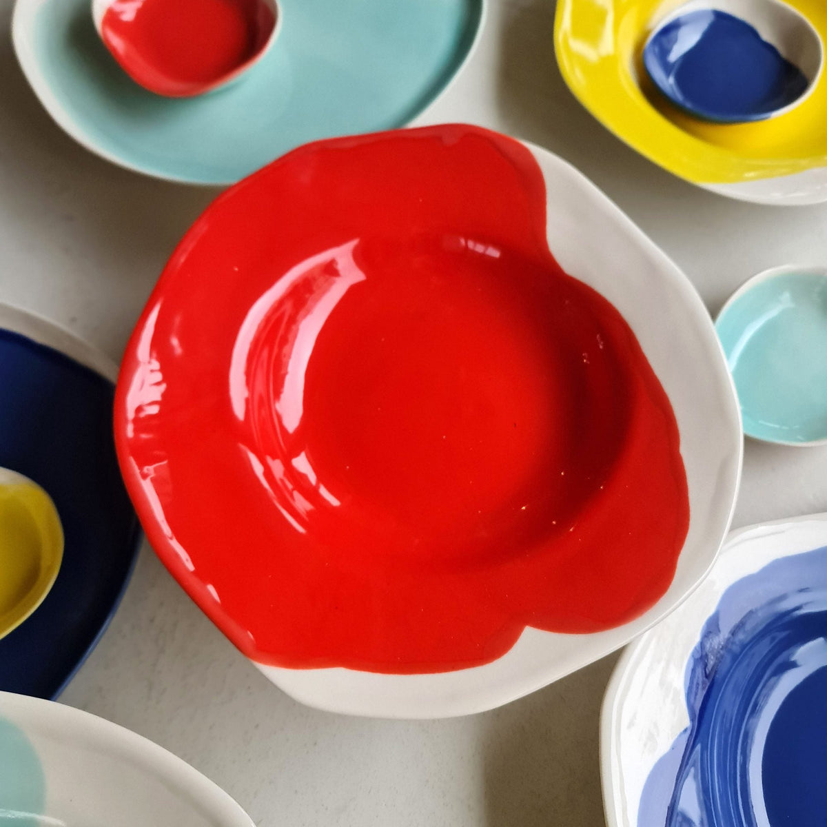 Red Scarlet porcelain plate among turquoise, yellow and blue glazed handmade dinnerware