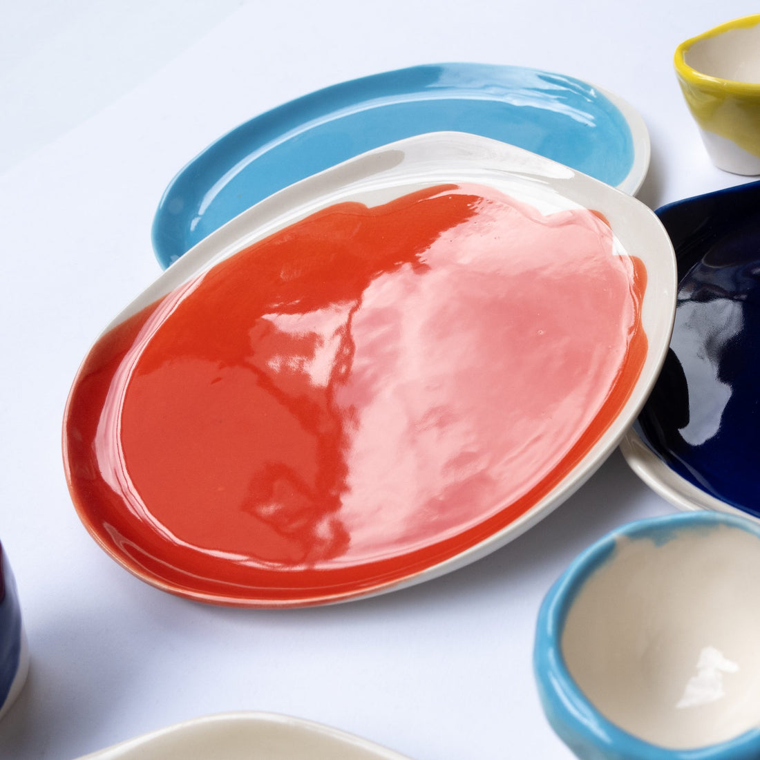 Oval handmade porcelain plate in Red Scarlet glaze among blue and turquoise ceramic dishes