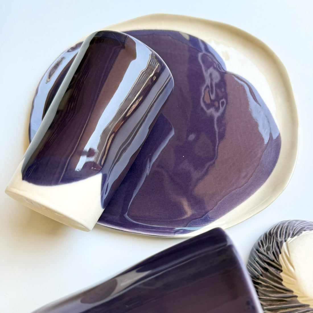 Aubergine glazed porcelain cup resting on a handmade plate with a wide white rim