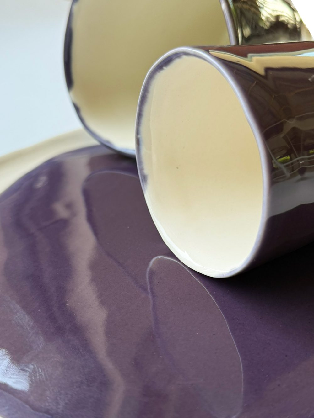 Porcelain cups with white interiors in glossy Aubergine glaze lying on a matching purple plate