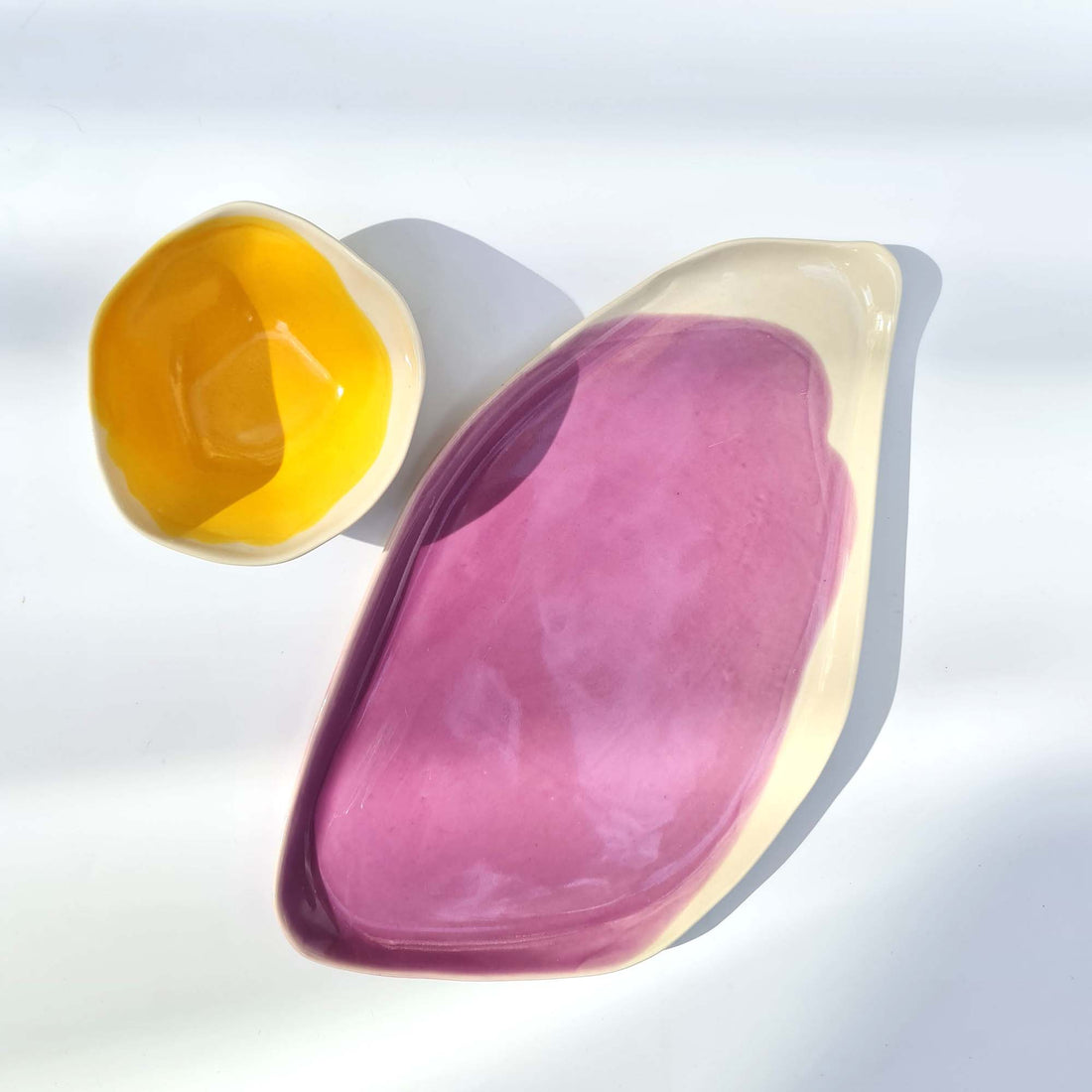 Oval porcelain serving plate in Orchid glaze next to a small yellow bowl in bright sunlight