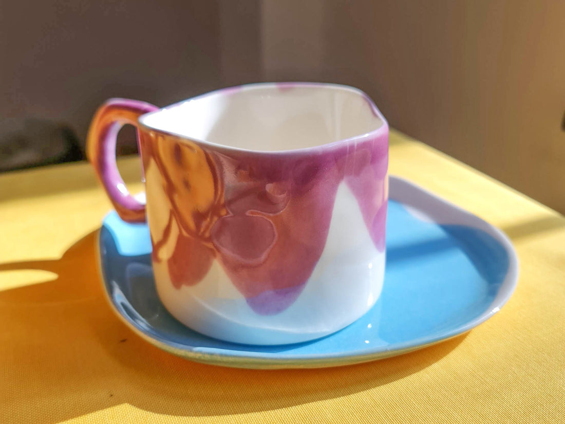 Porcelain cup in Orchid glaze with a sculpted handle on a sky blue saucer in warm sunlight