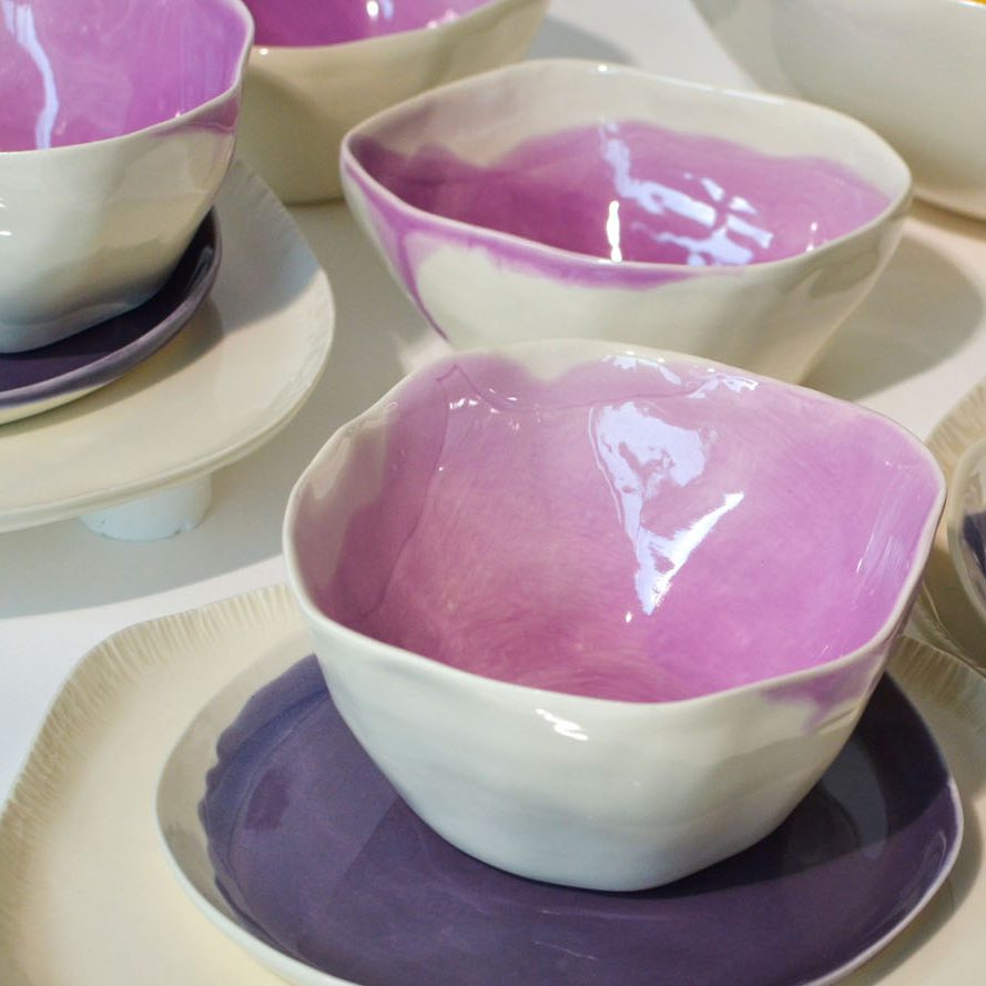 Handmade porcelain bowls with Orchid glaze interiors and white exteriors on purple and ivory plates