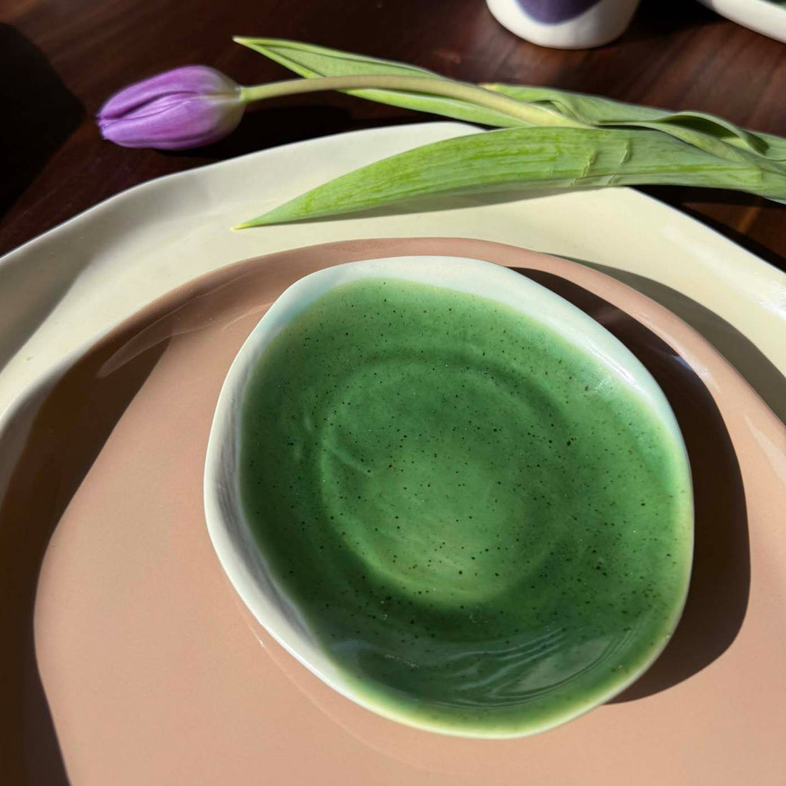 Speckled Kiwi Green glazed ceramic bowl set on a blush pink handmade porcelain plate with a lilac tulip