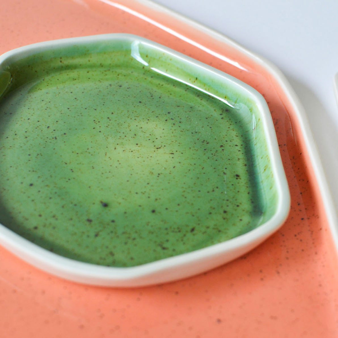 Hexagonal porcelain plate in speckled Kiwi Green glaze on a coral pink tray