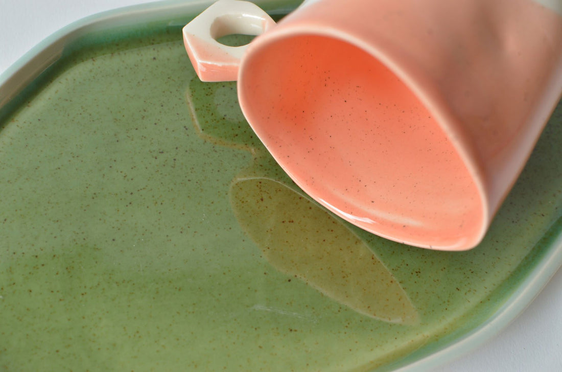 Coral pink porcelain cup lying on a speckled Kiwi Green glazed plate, handmade tableware