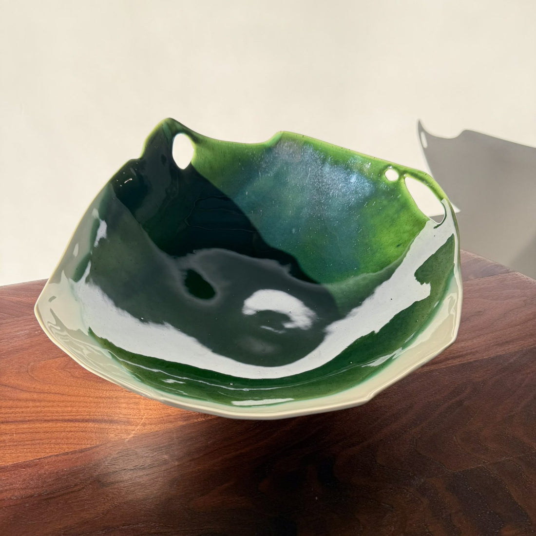 Organic handmade porcelain bowl in deep Moss Green glaze with a pierced rim on a wooden table