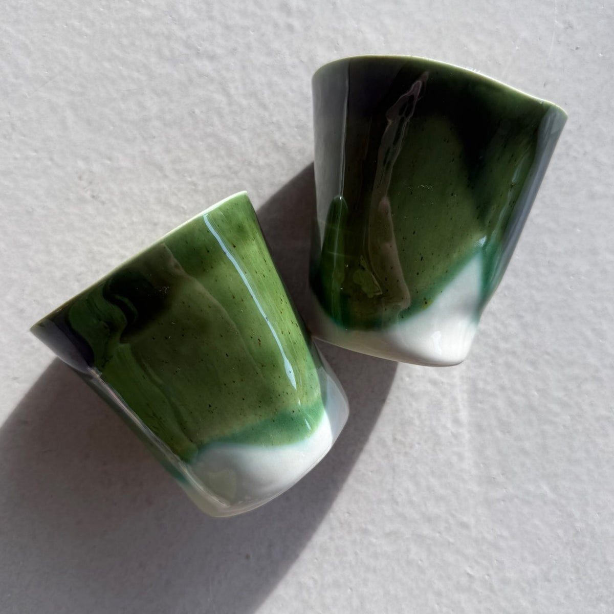 Two handmade porcelain cups in Moss Green glaze with white dipped bases on a white surface