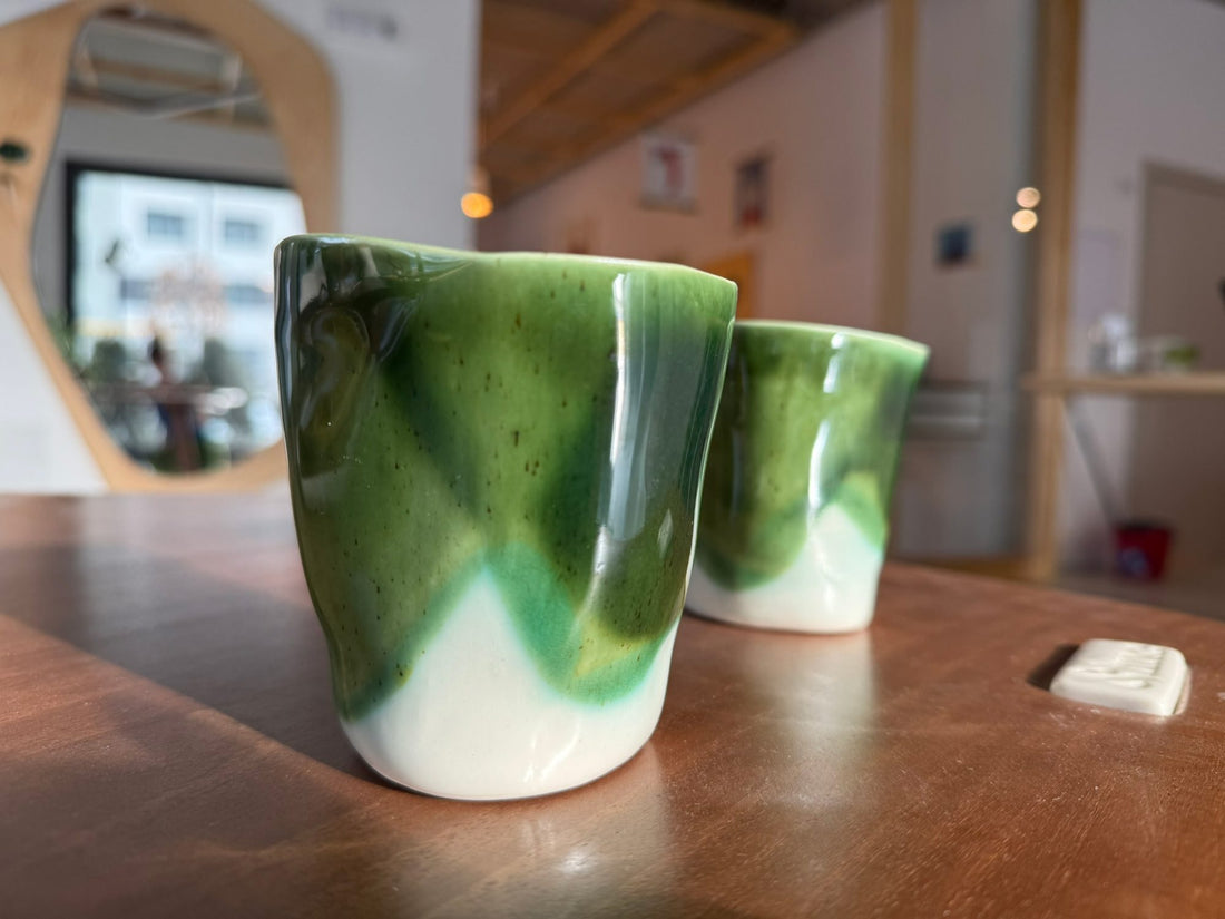 Porcelain cups in Moss Green glaze over white standing on a cafe counter