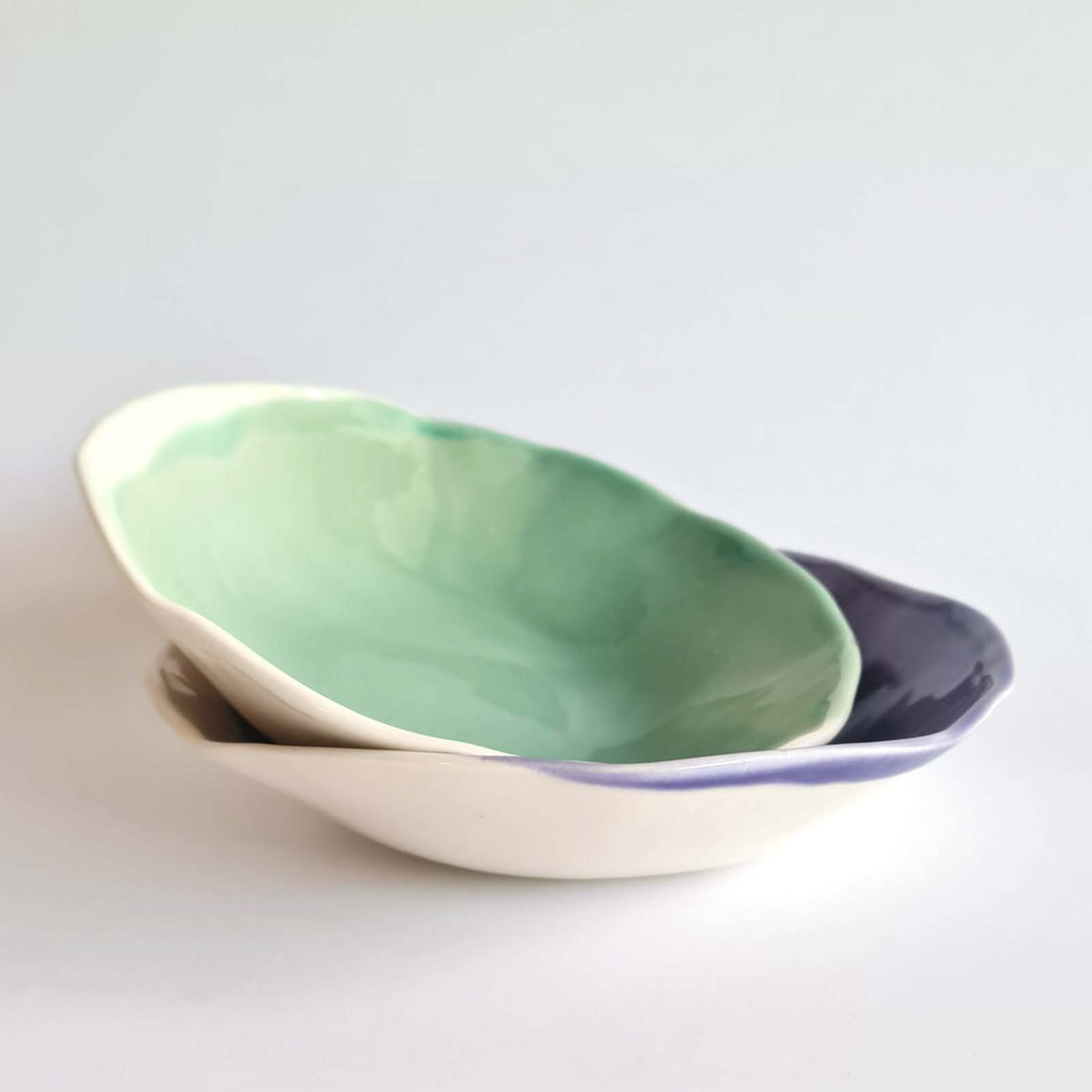 Two nested handmade porcelain bowls in Sage Green and deep violet glaze on a white background