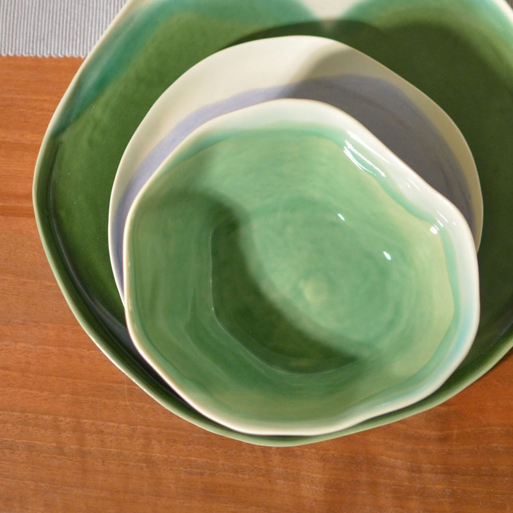 Stacked handmade ceramic bowls in Sage Green glaze with an organic wavy rim on a wooden table
