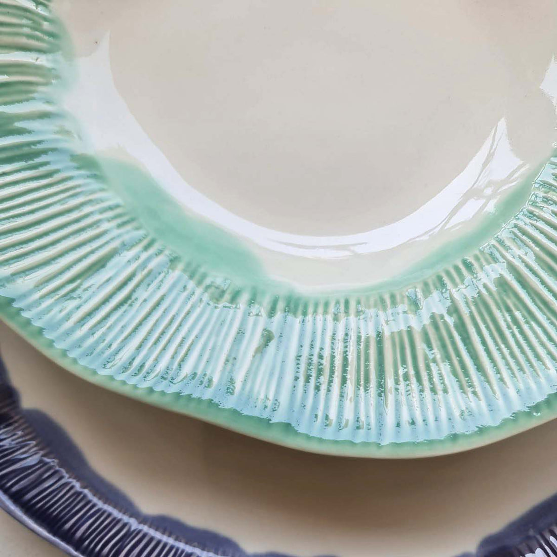 Textured handmade porcelain plate with a glossy Sage Green glaze rim over a dark blue plate