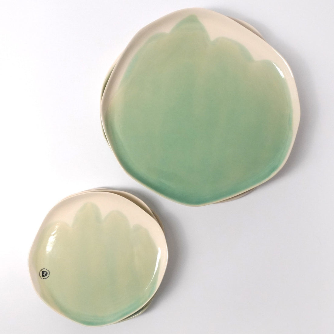 Two handmade porcelain plates with scalloped Sage Green and pale cream glaze, seen from above