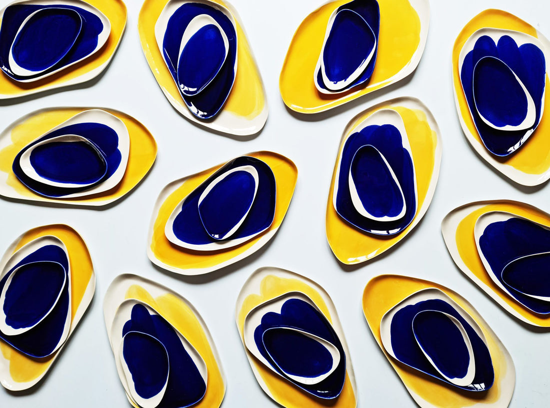Rows of oval porcelain plates in Royal Blue and yellow glaze arranged on a white surface