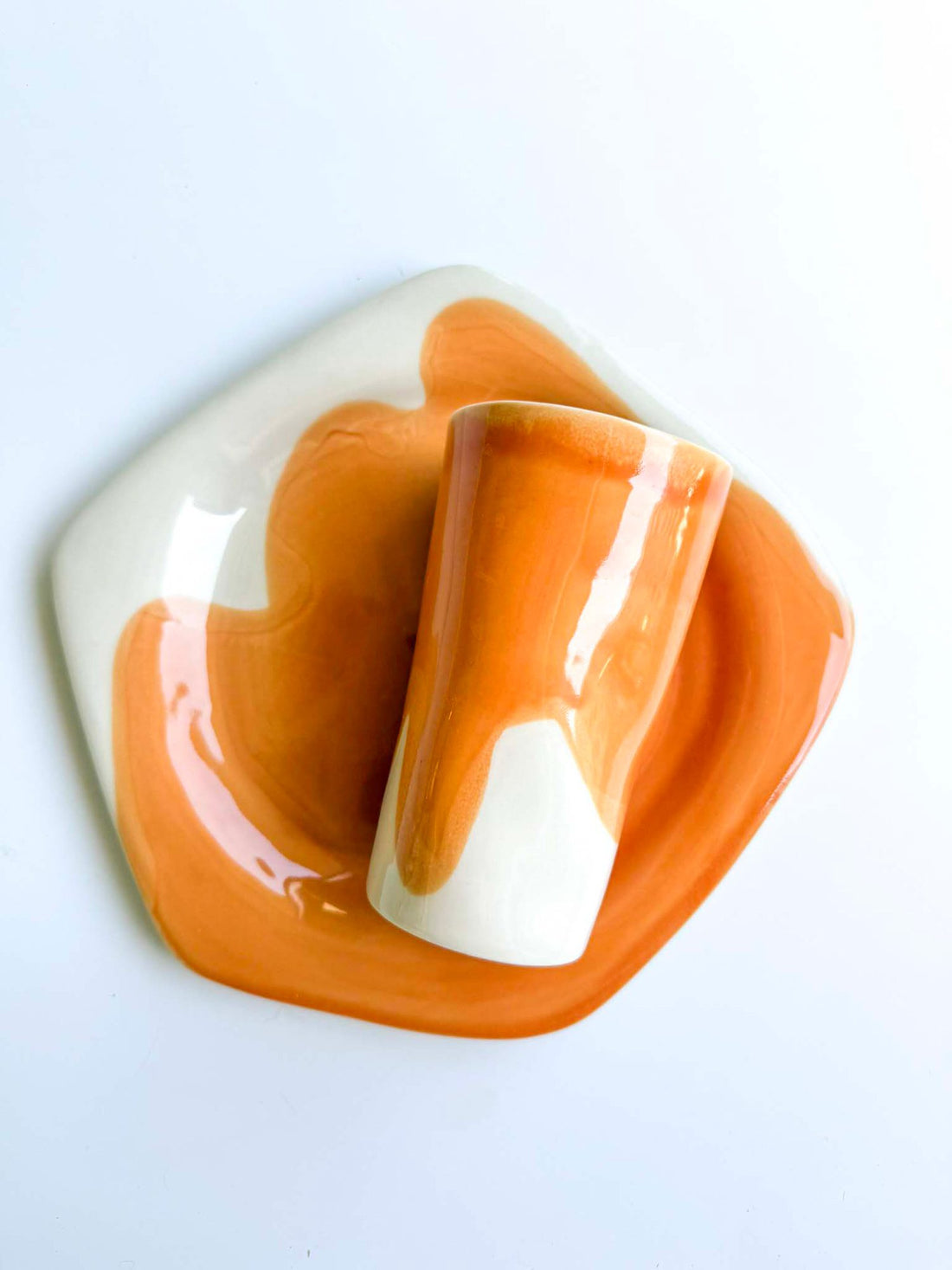 Porcelain cup and wavy saucer in Saffron glaze over white, handmade tableware on a pale background