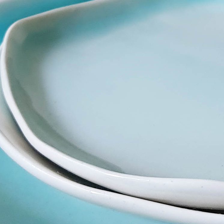 Close-up of stacked handmade porcelain plates in soft Turquoise glaze with raw white rims