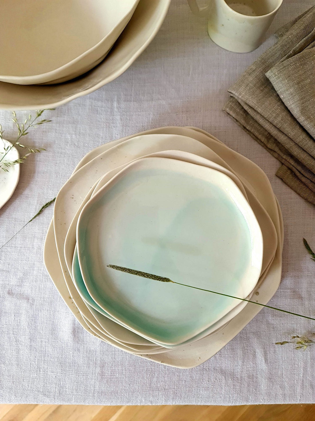 Stack of organic handmade porcelain plates in pale Turquoise glaze on a linen tablecloth